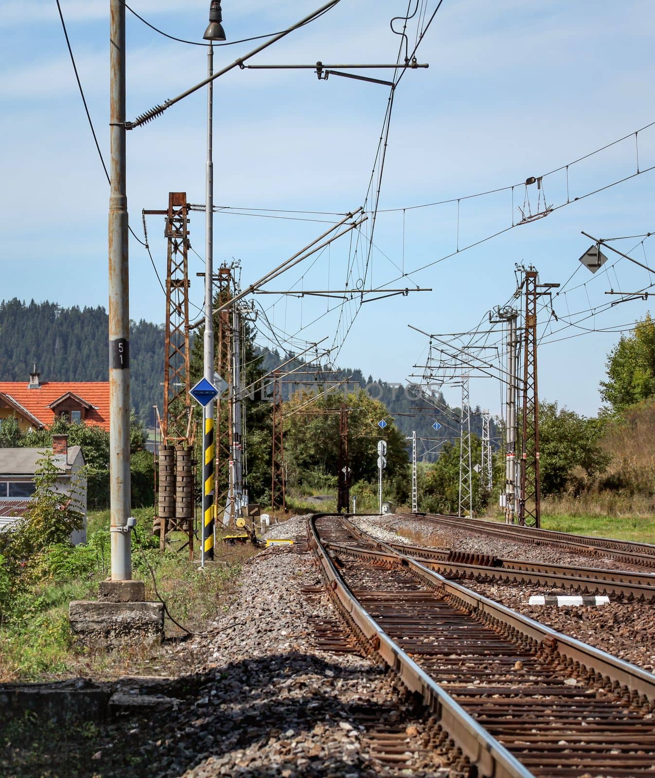 Empty railway tracks on a sunny summer day, in rural area, pillars with many electric cables around. by Ivanko