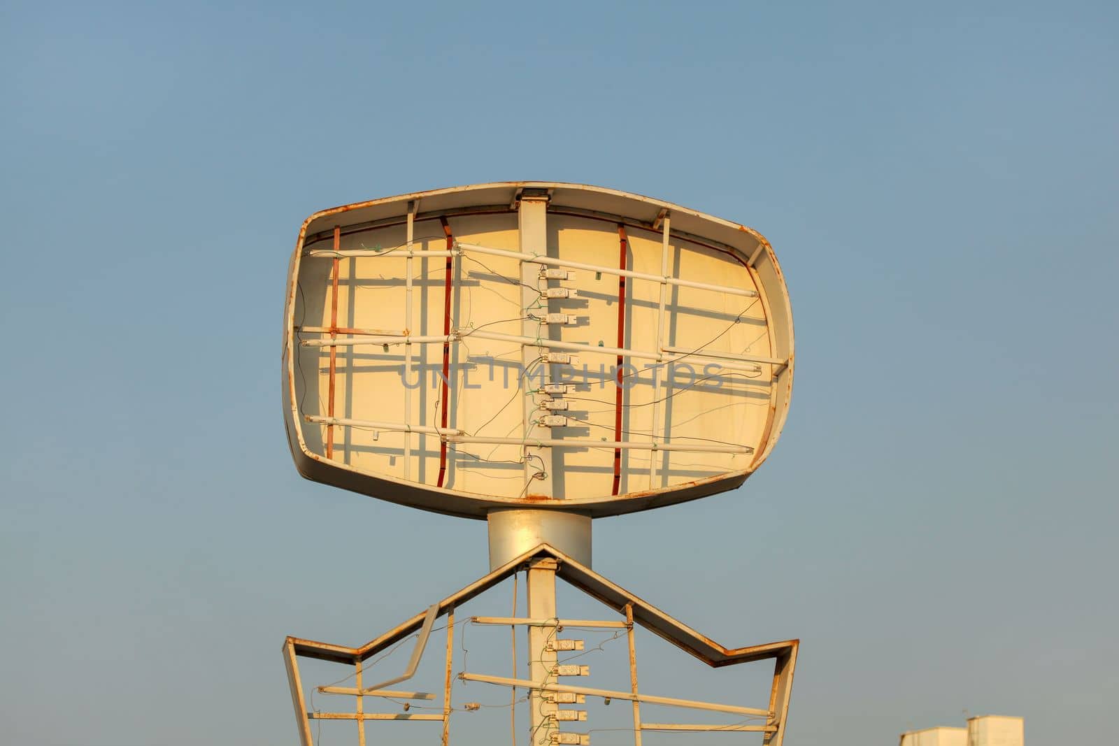 Empty neon advertising sign, tubes visible, clear afternoon sky in background.