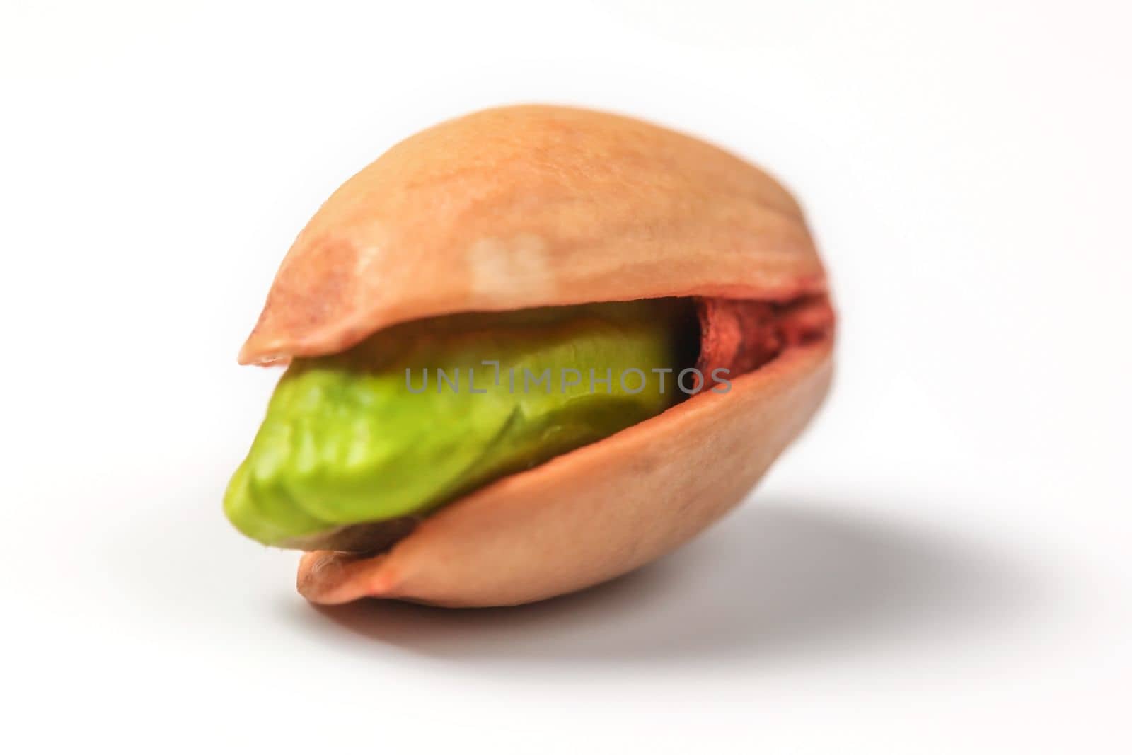 Single red Turkish pistachio, green nut visible under shell, isolated on white background. 