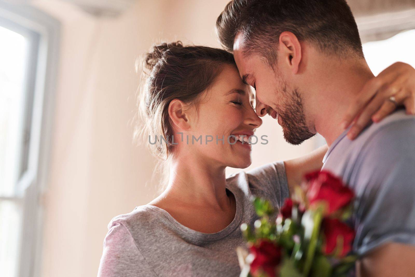 Keep the romance alive in your relationship. a young man surprising his girlfriend with a bunch of roses in their bedroom at home. by YuriArcurs