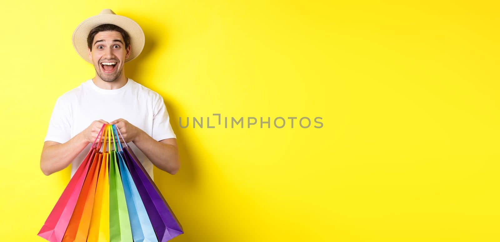 Image of happy man shopping on vacation, holding paper bags and smiling, standing against yellow background by Benzoix