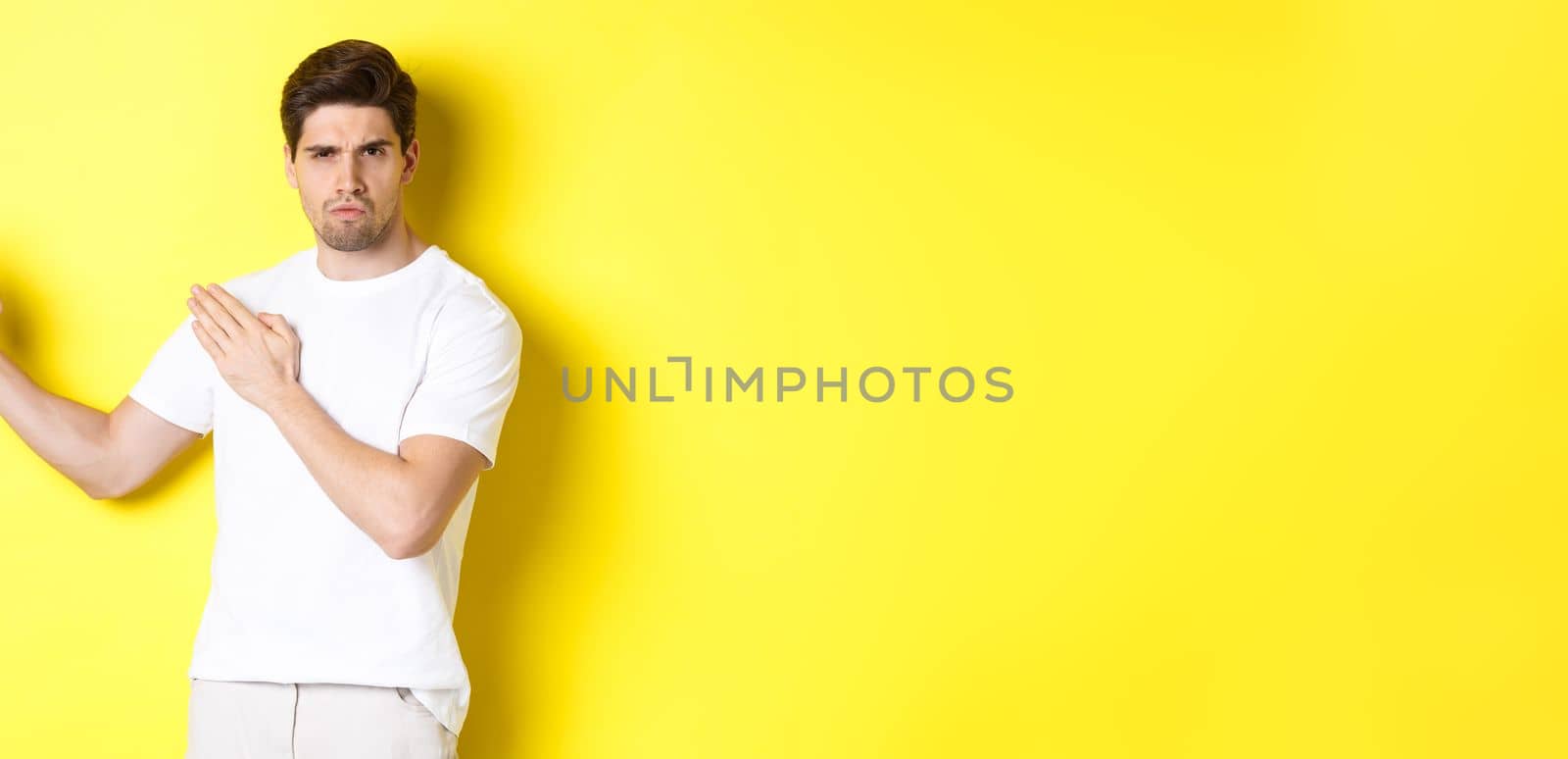 Man showing kung-fu skills, martial arts ninja movement, standing in white t-shirt ready to fight, standing over yellow background. Copy space