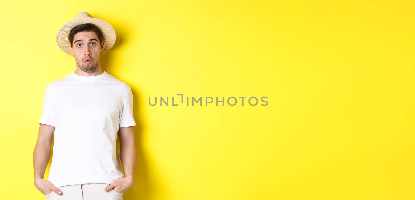 Confused guy traveller in straw hat looking puzzled, stare at camera, standing over yellow background. Copy space