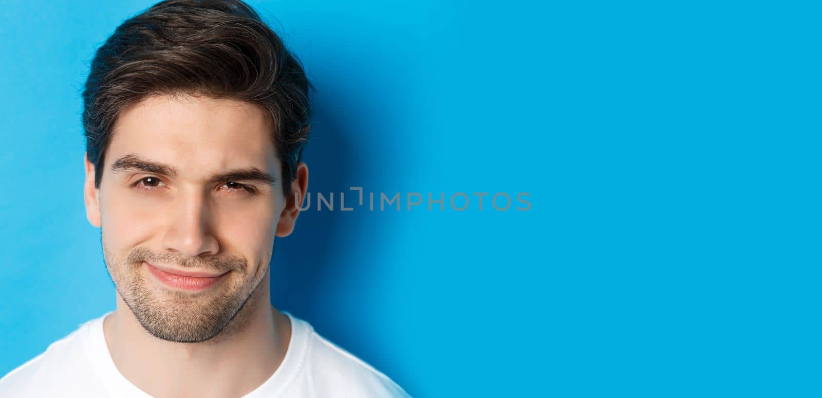 Headshot of thoughtful handsome man, looking intrigued and squinting, thinking about something, standing over blue background.