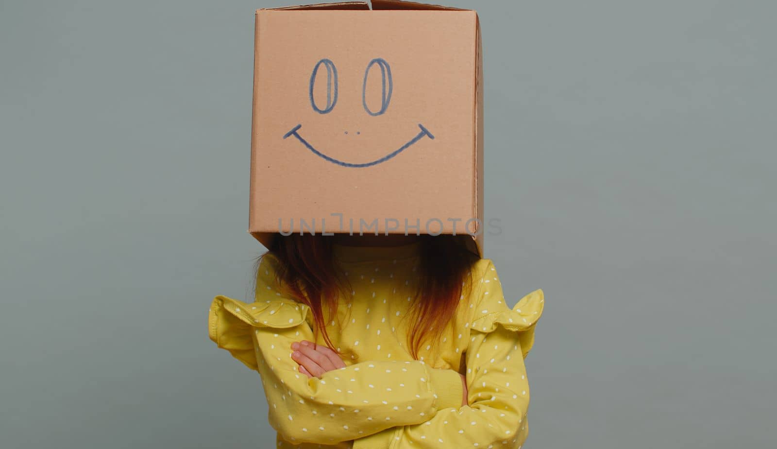 Young toddler girl in glasses frustrated after quarrel, ignores and does not want to communicate, talk. Preteen female child kid wearing cardboard box with smiling face to change mood. Little children