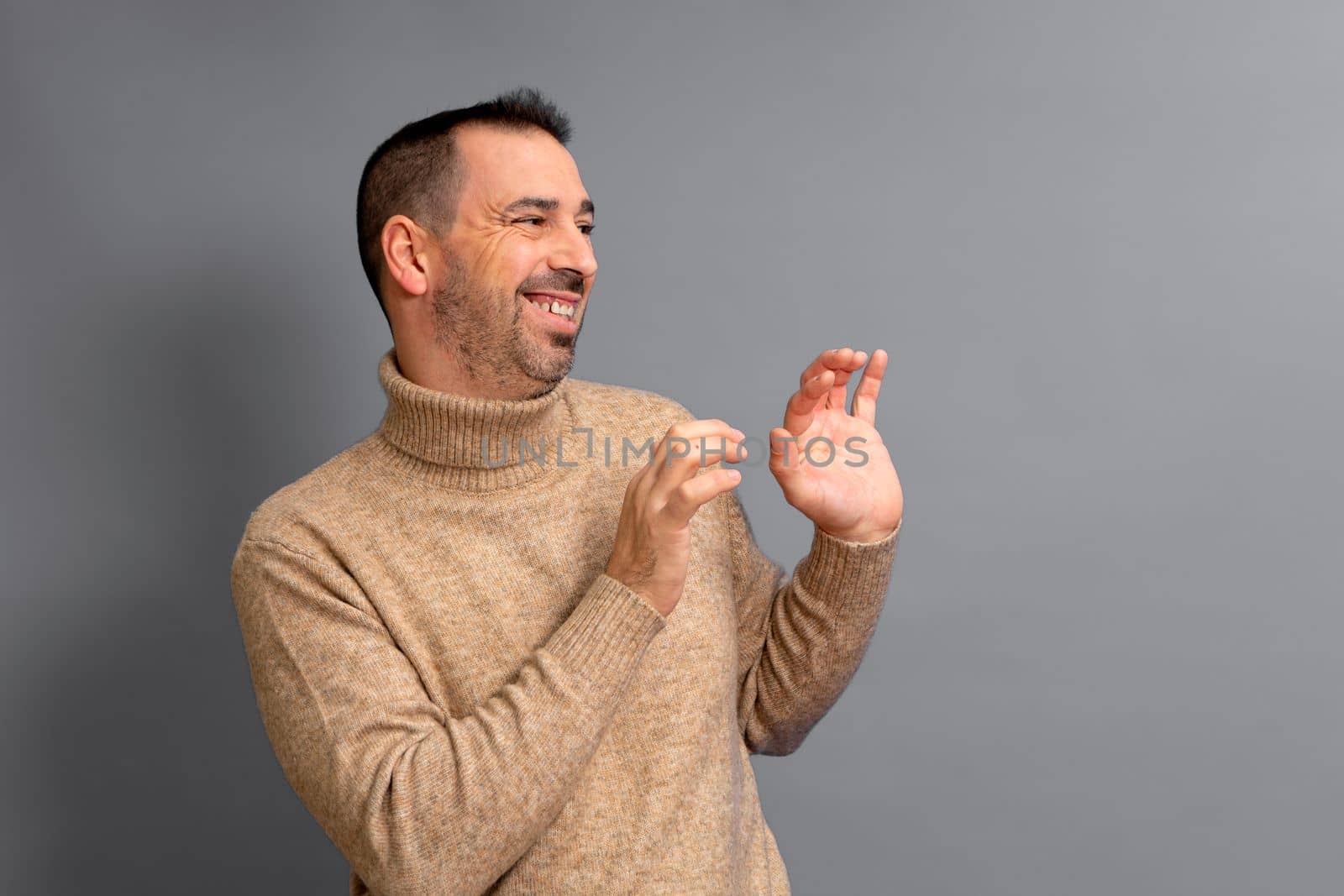 Bearded hispanic man wearing a turtleneck pulled to the side with his hands in front in a gesture of embarrassment and shyness, isolated over gray background