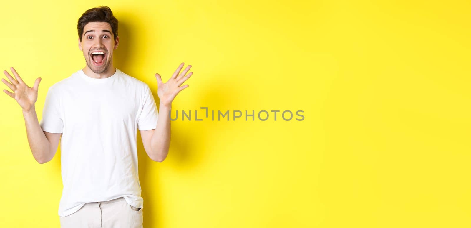 Portrait of excited and surprised man reacting to big promo offer, shouting for joy and triumphing, standing over yellow background.