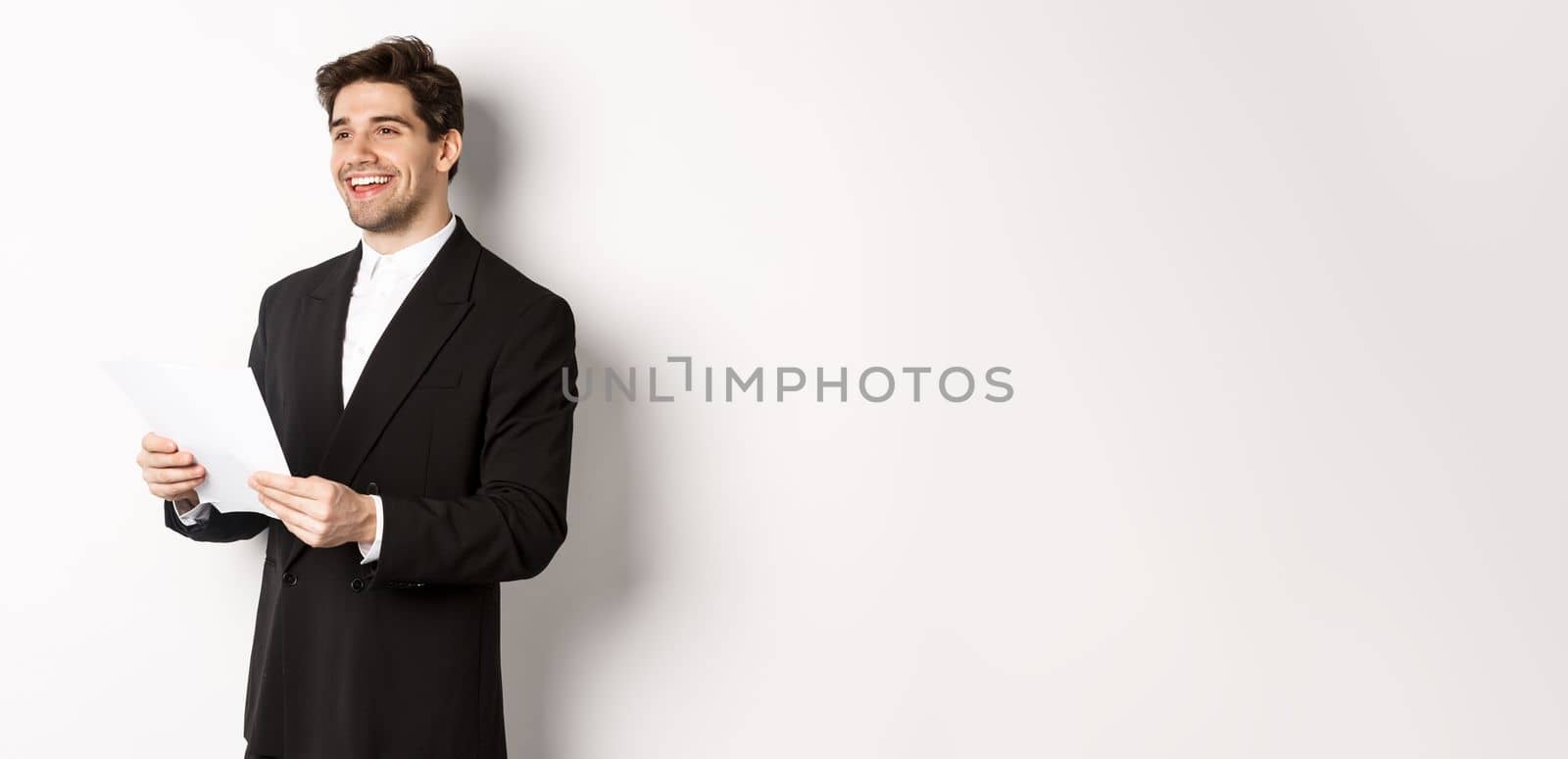 Image of handsome businessman in suit, holding documents and smiling, standing against white background by Benzoix