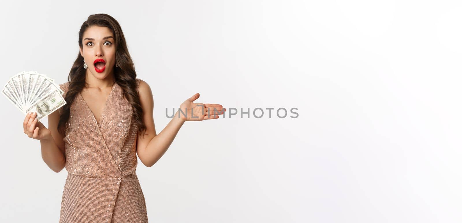 Shopping concept. Elegant woman in glamour dress holding money and looking surprised. winning prize, standing over white background.