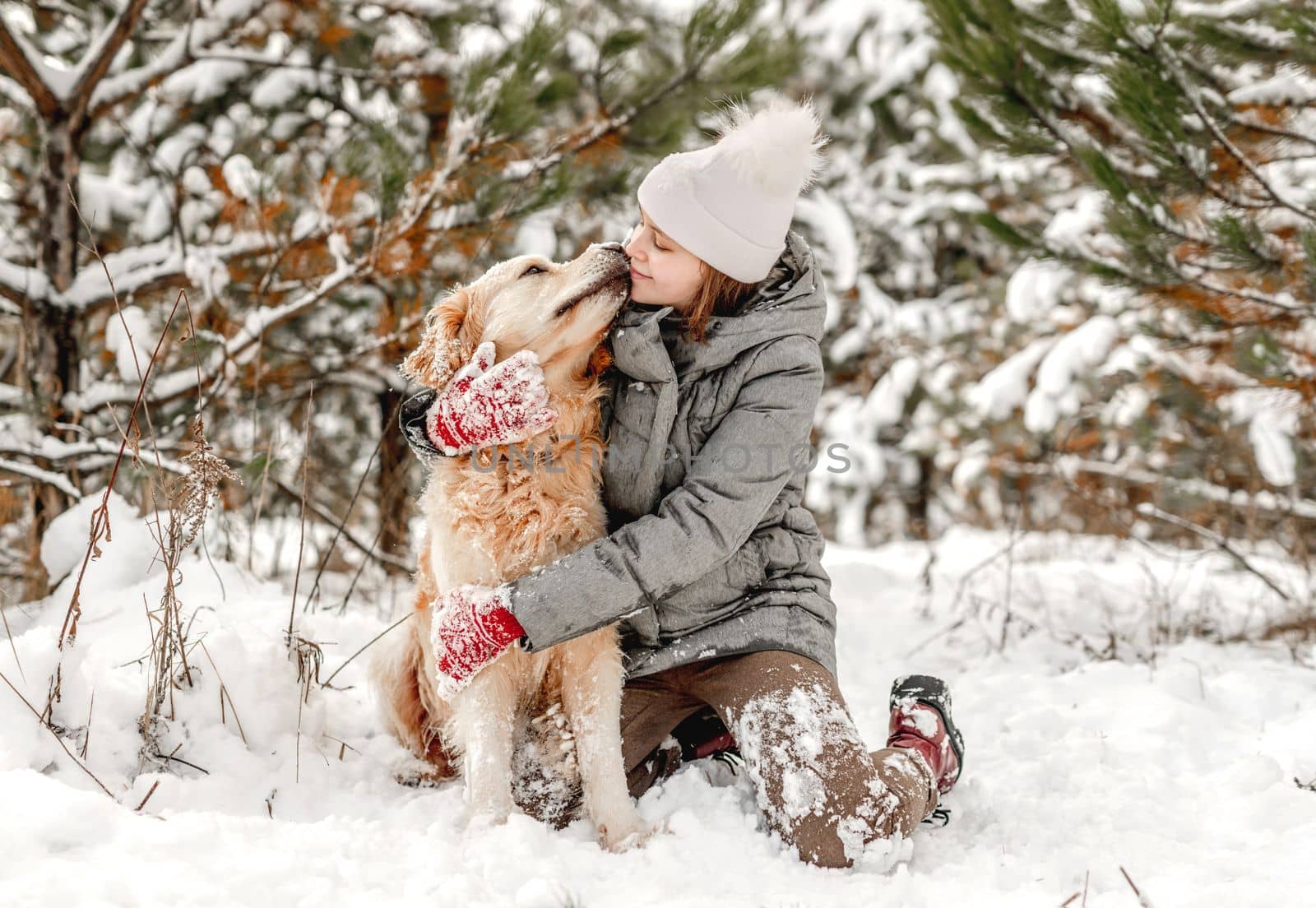 Girl petting and hugging golden retriever dog sitting in snow in winter time. Young woman with doggy pet outdoors in cold weather with snowflakes