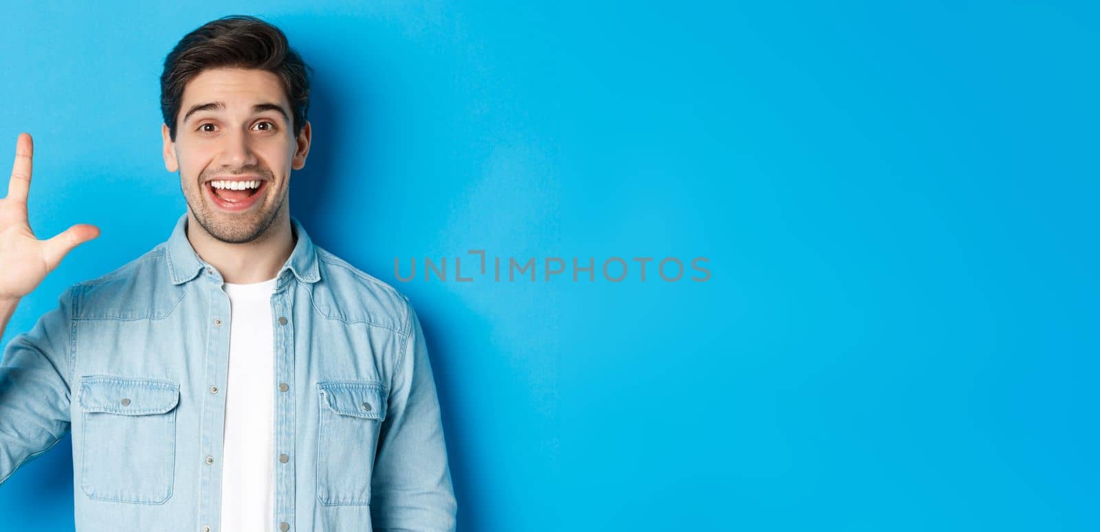 Close-up of handsome man smiling, showing fingers number five, standing over blue background by Benzoix