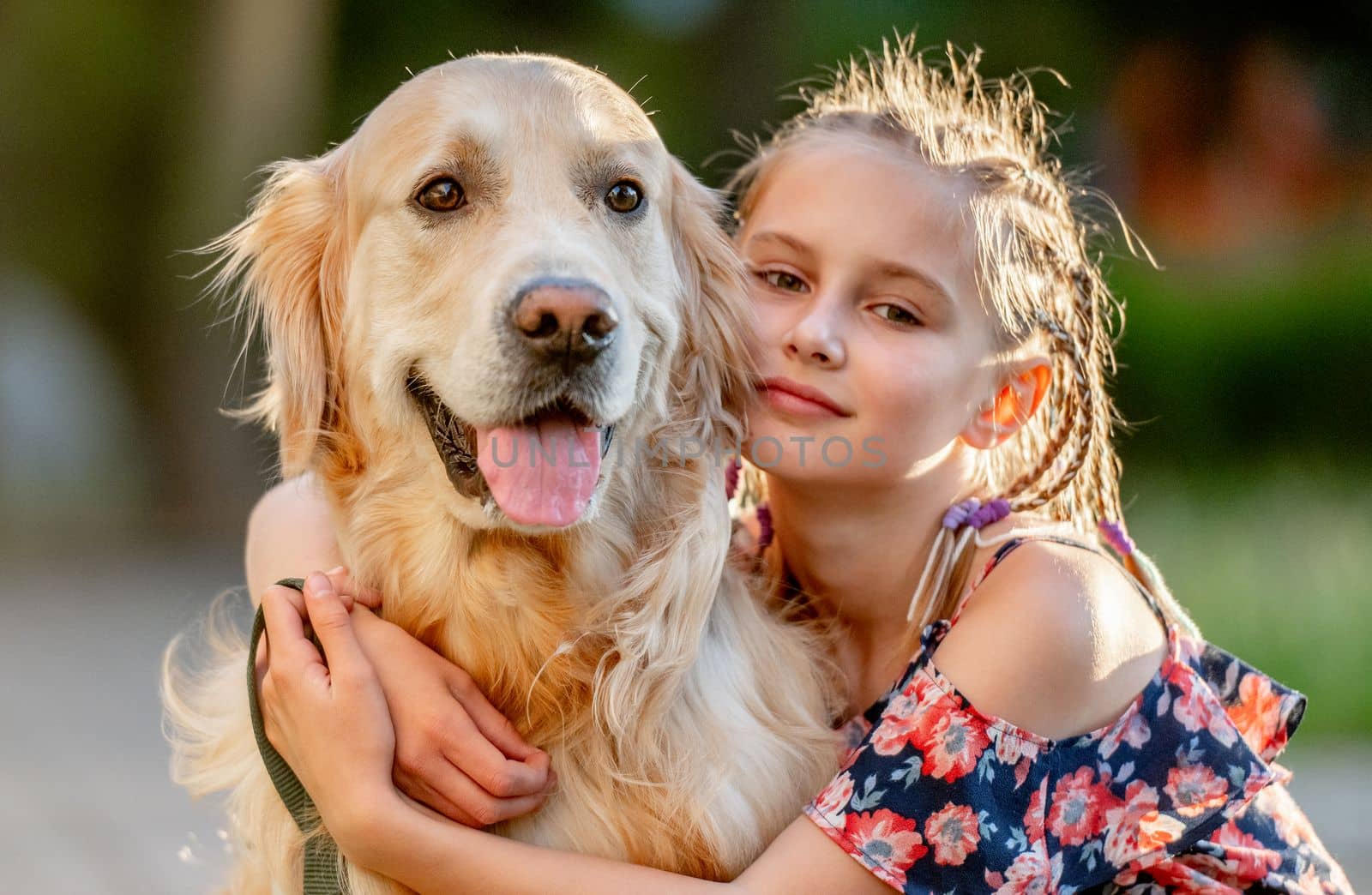 Preteen girl with golden retriever dog sitting in park in beautiful summer day. Adorable female child kid hugging purebred doggy pet outdoors portrait