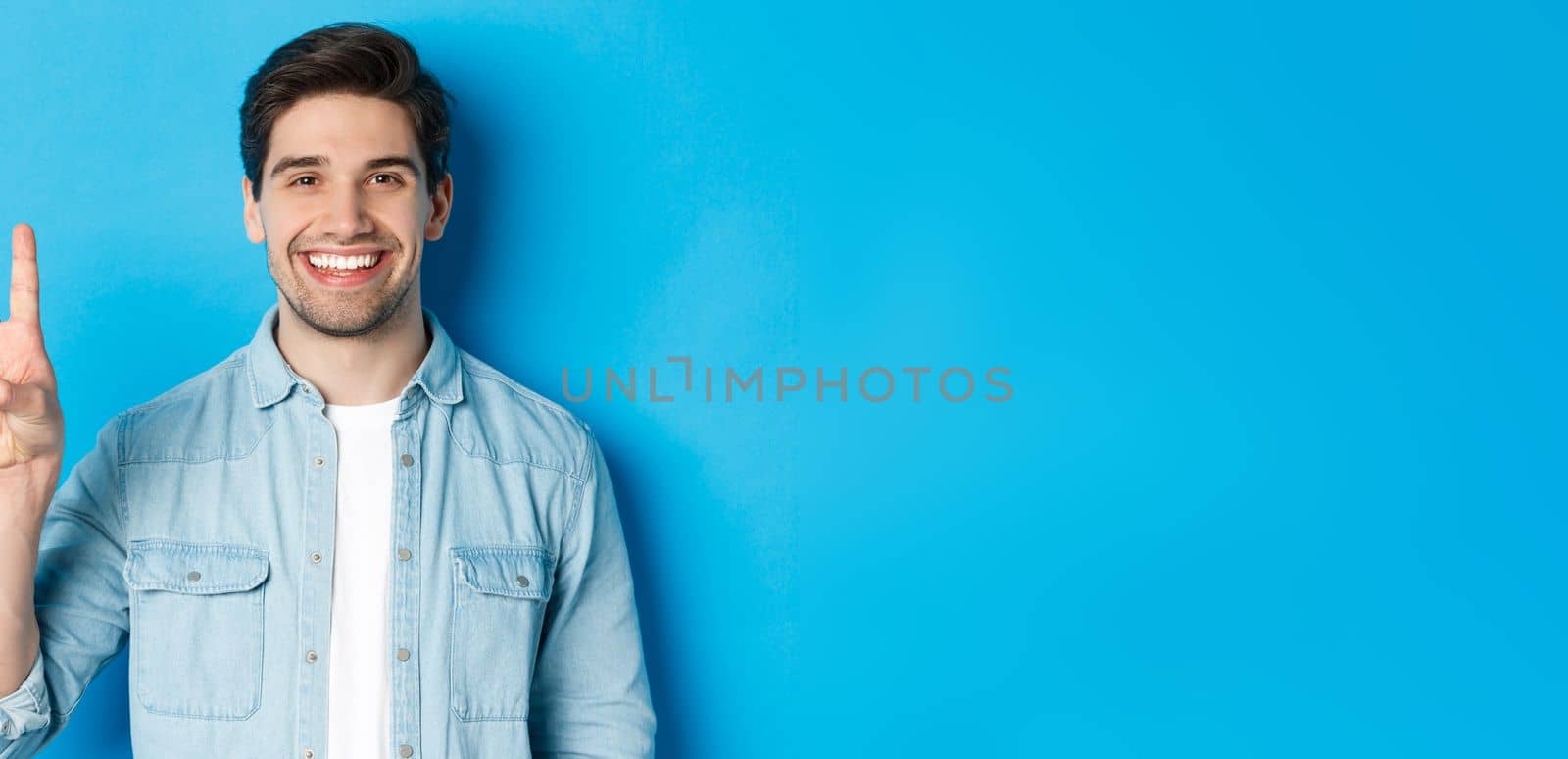 Close-up of handsome man smiling, showing fingers number three, standing over blue background.