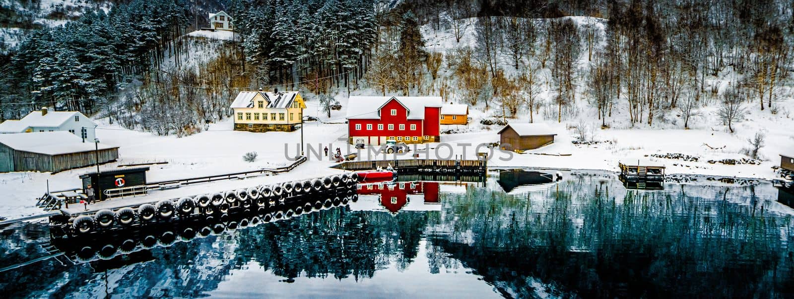 Charming village in Norway with wooden red houses surrounded with snowy mountains and lake with reflection in winter. Scenery scandinavian landscape with sea view in Europe