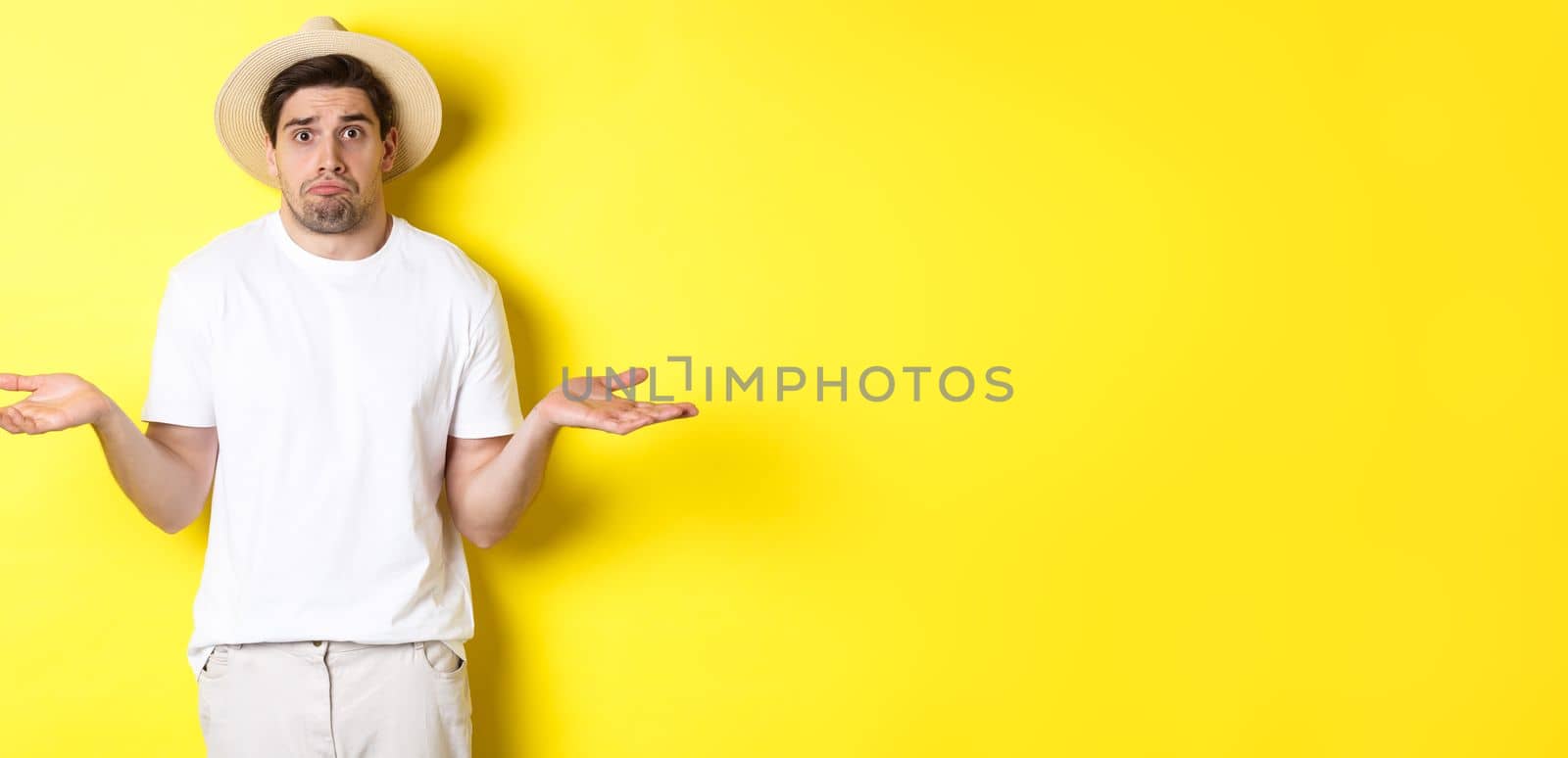 Concept of tourism and summer. Confused male tourist shrugging, looking indecisive, standing against yellow background.