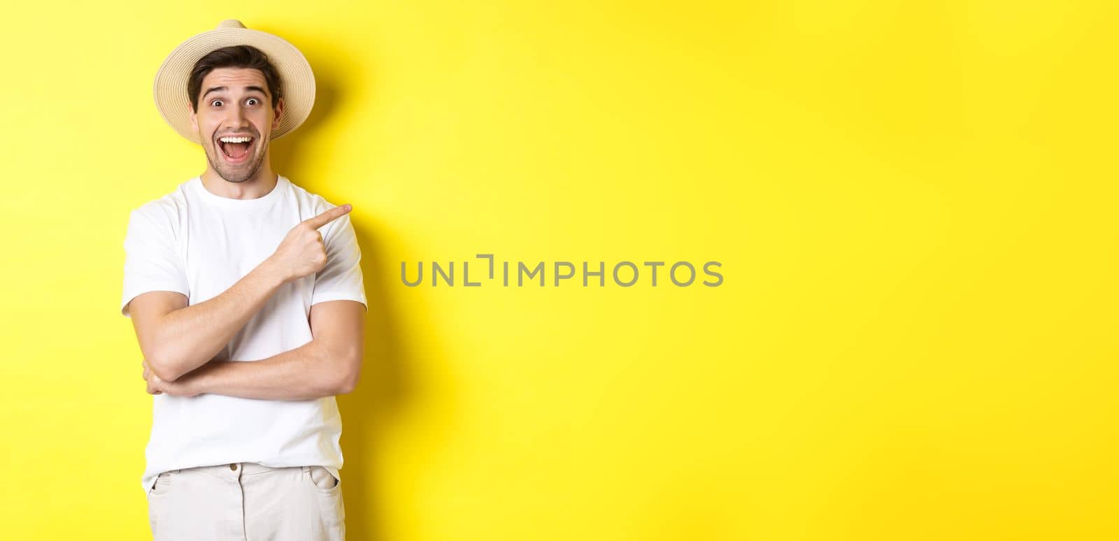 Happy male tourist in straw hat pointing finger right, showing promo offer on copy space, yellow background by Benzoix