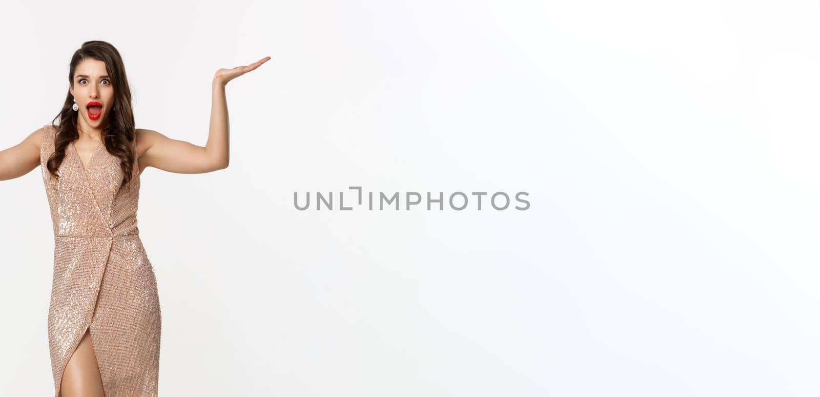 Party and celebration concept. Full-length of beautiful woman in elegant dress, standing near Christmas gifts and looking surprised, standing over white background.