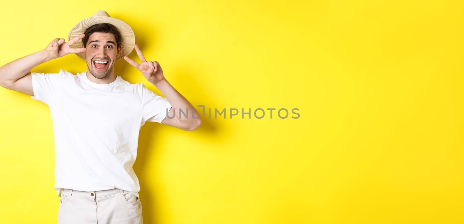 Concept of tourism and vacation. Happy man tourist posing for photo with peace signs, smiling excited, standing against yellow background.