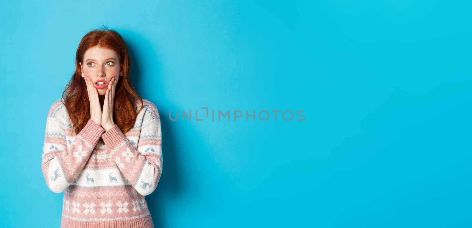 Image of shocked and impressed redhead girl realise something, staring left amazed, standing over blue background.