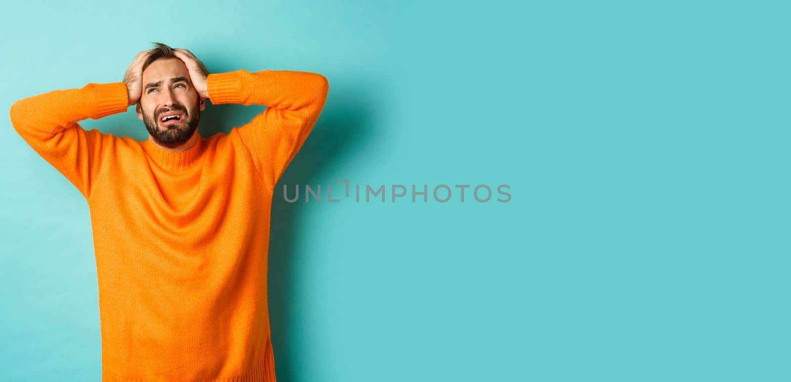 Frustrated and desperate man holding hands on head, looking sad and distressed, standing tensed over light blue background.