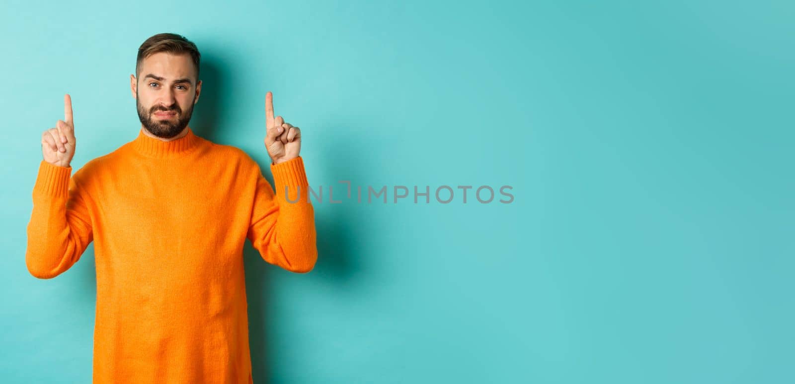 Skeptical and reluctant man looking displeased, pointing fingers up, bad offer, standing over turquoise background by Benzoix