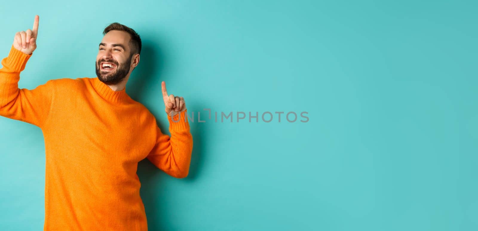 Handsome man celebrating, feeling winner, pointing fingers up and do champion dance, standing over light blue background.