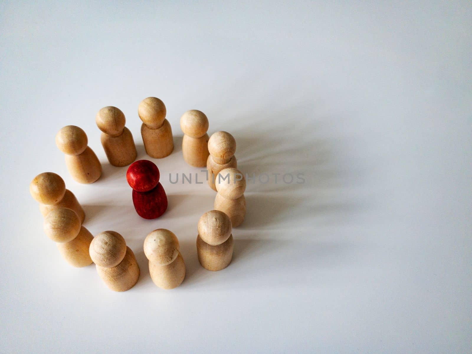 Red wooden doll figure surrounded by other doll figure on white background. Harassment and bully concept.