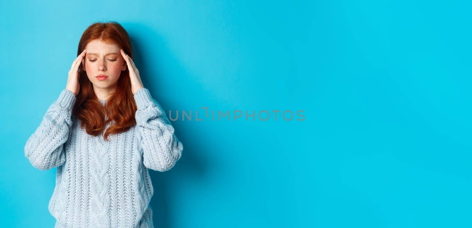 Distressed teenage redhead girl touching head, looking down with troubled face expression, standing against blue background, have problem by Benzoix