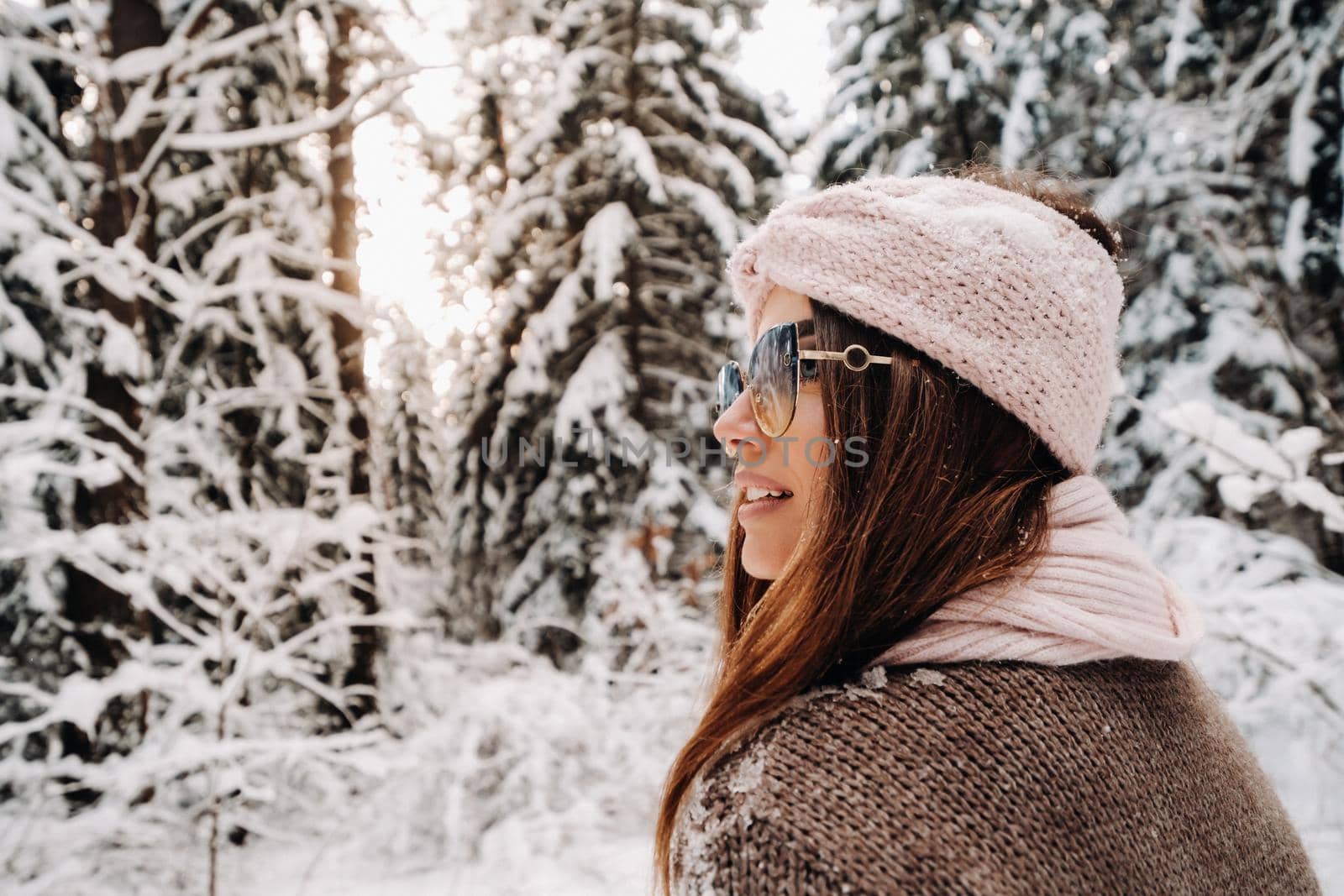 A girl in a sweater and glasses in winter in a snow-covered forest.