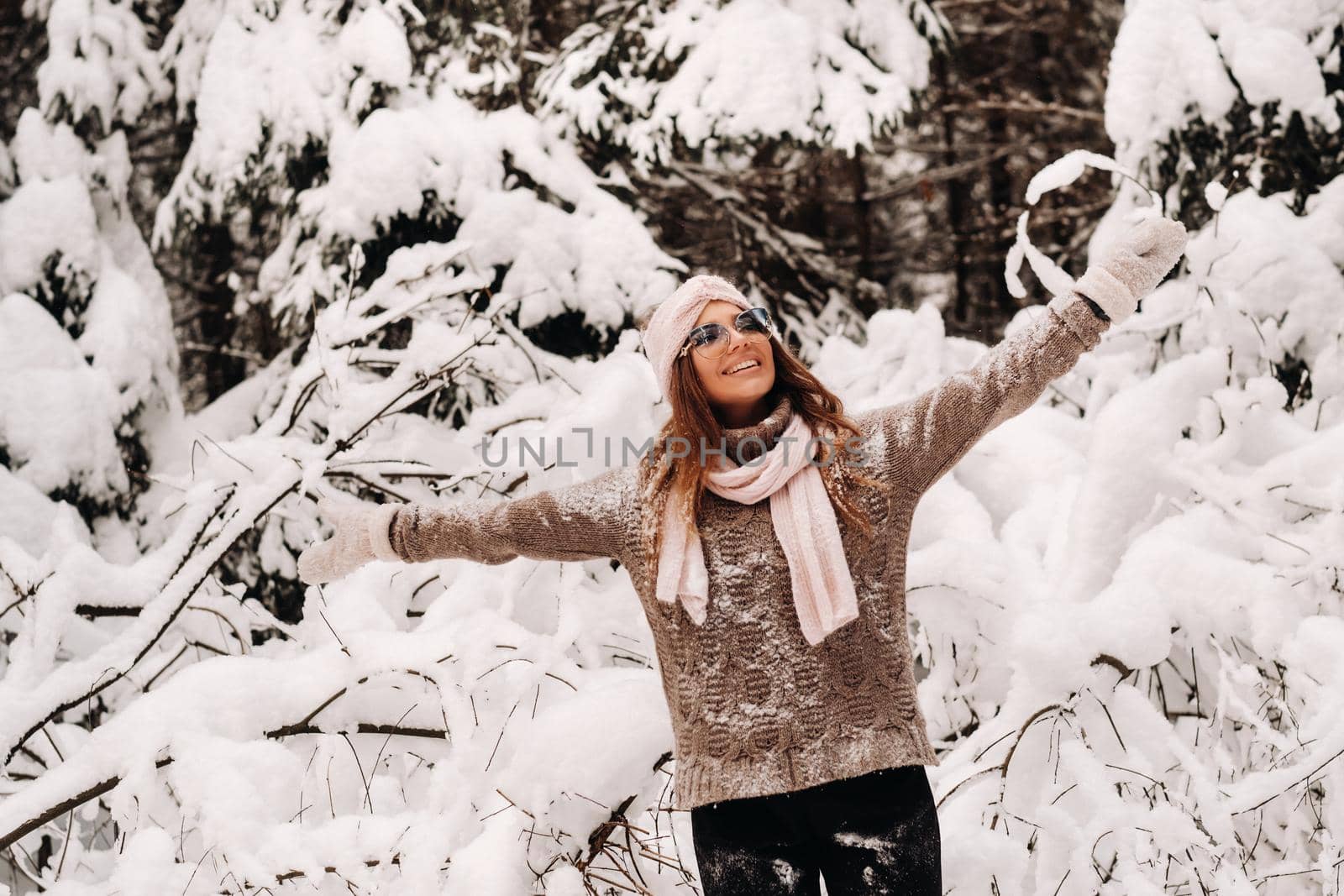 A girl in a sweater and glasses in winter in a snow-covered forest.