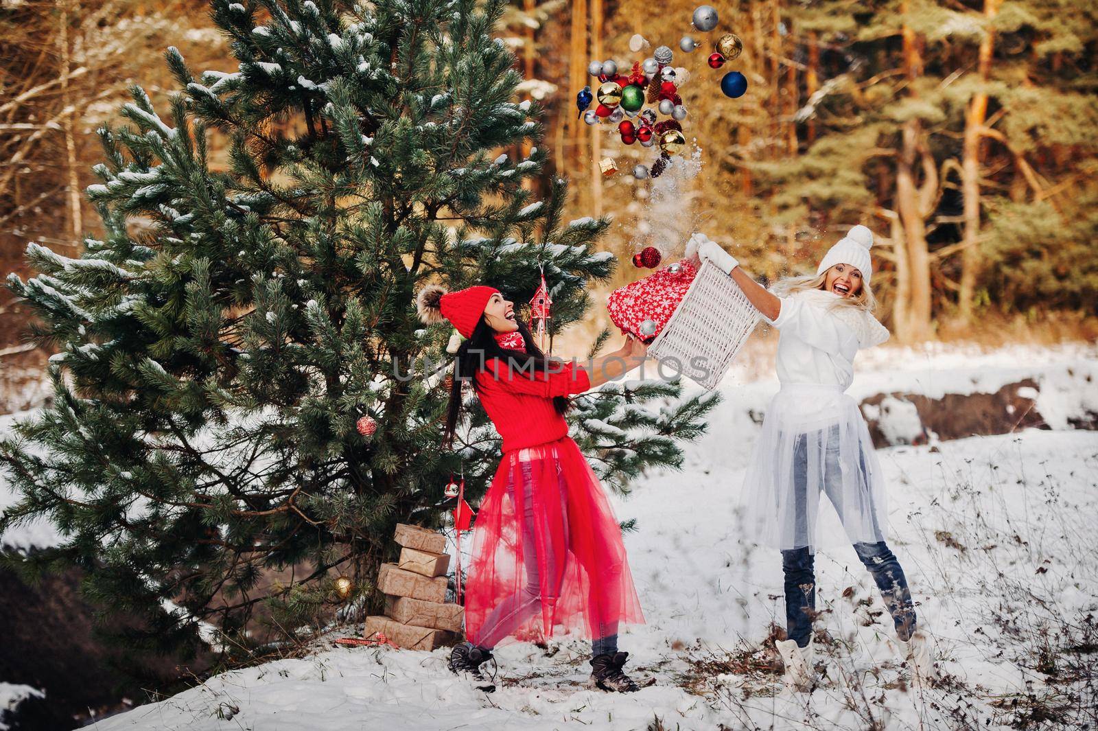 two girls near the Christmas tree throw a lot of toys on the tree. Christmas tree decoration on the street in winter.Lots of Christmas balls on the tree by Lobachad