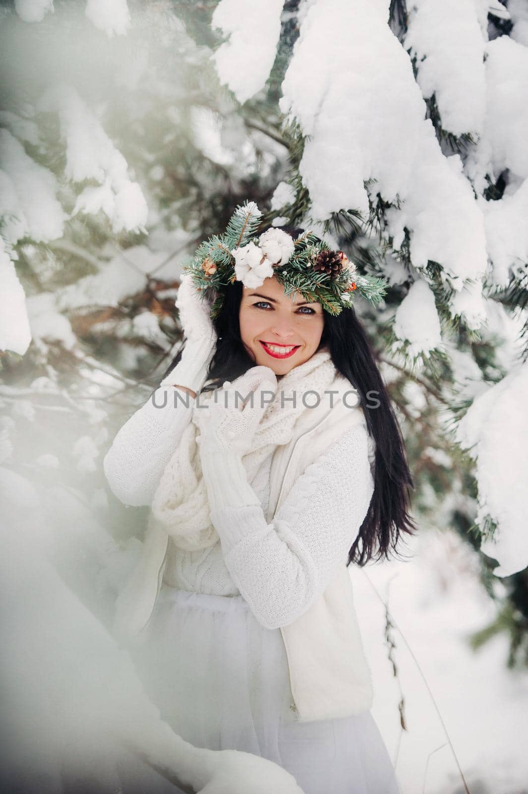 Portrait of a woman in white clothes in a cold winter forest. Girl with a wreath on her head in a snow-covered winter forest.
