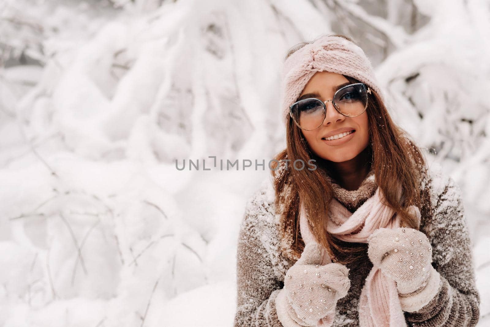 A girl in a sweater and glasses in winter in a snow-covered forest.