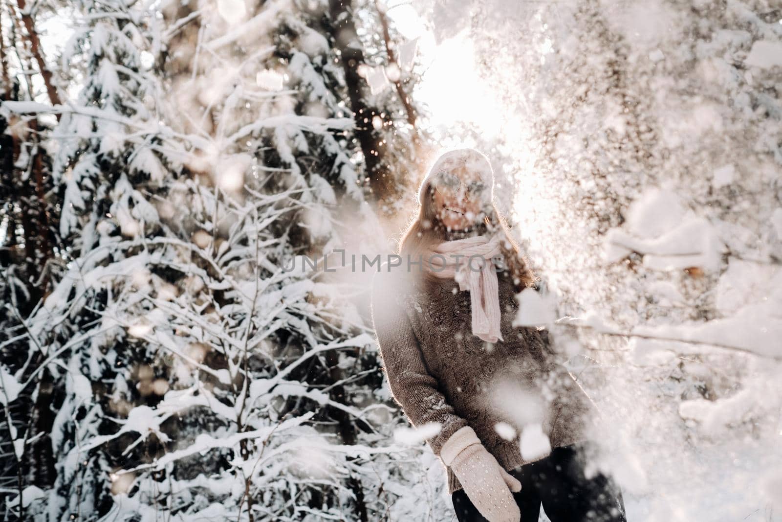 A girl in a sweater and glasses in winter in a snow-covered forest.