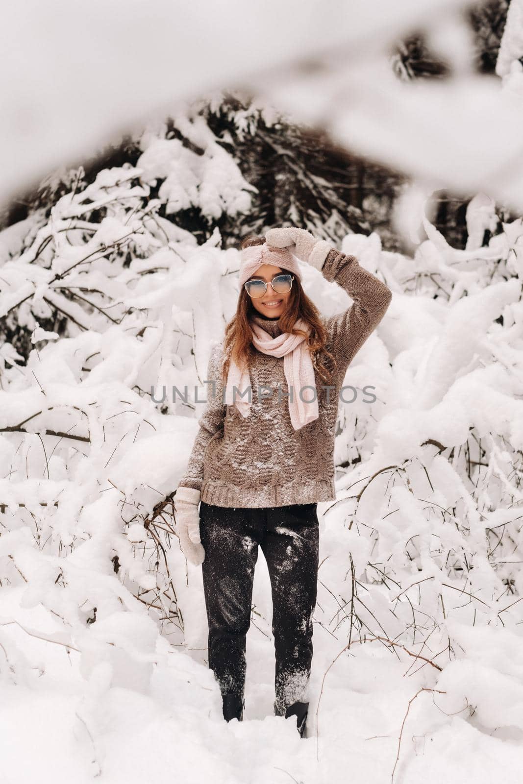 A girl in a sweater and glasses in winter in a snow-covered forest.