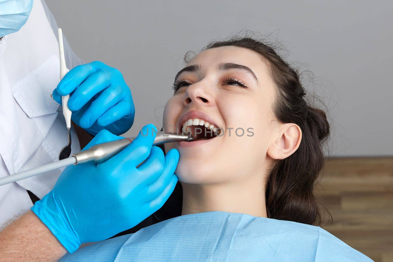 Lady patient sitting in stomatology chair, dentist drilling tooth, modern clinic