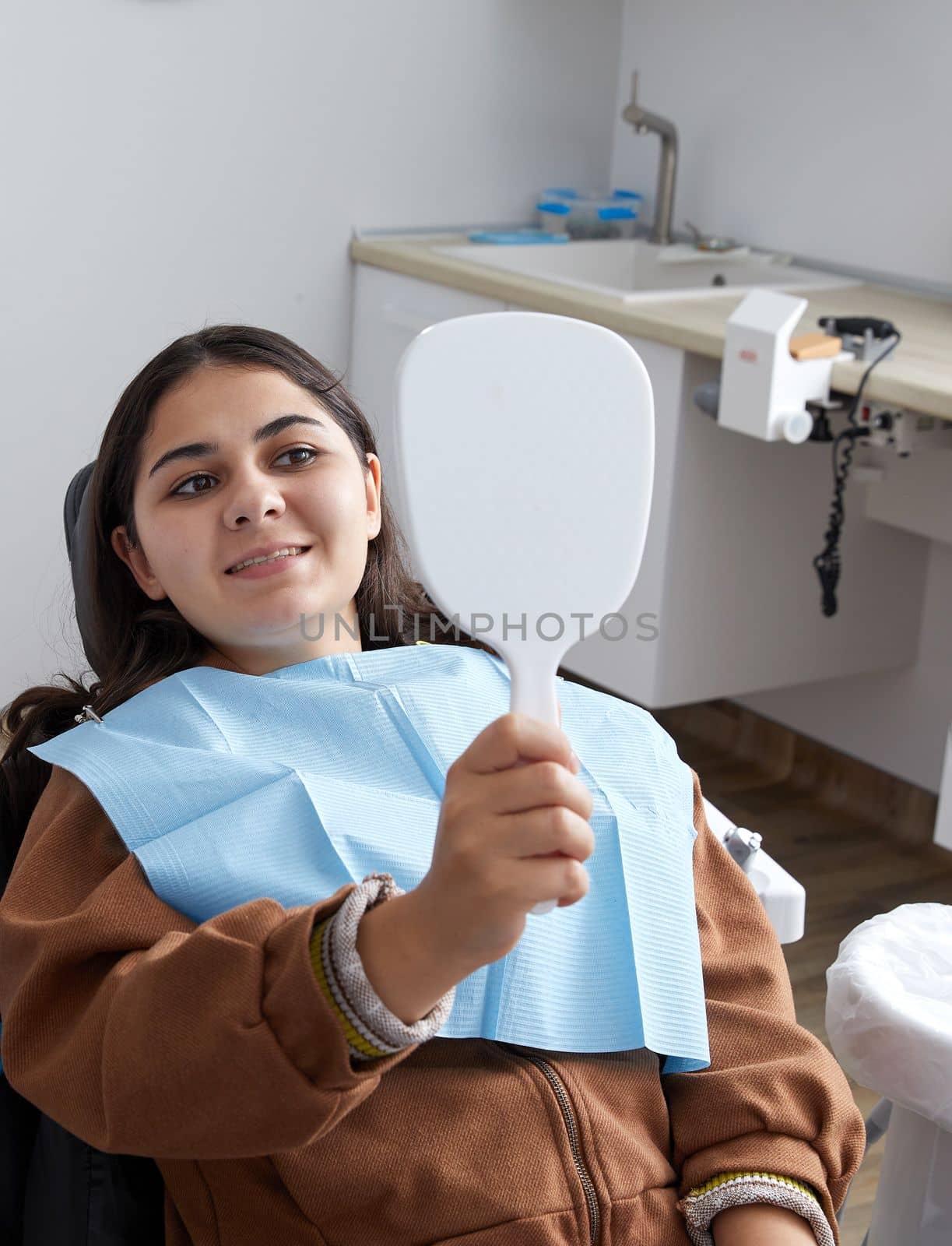 Young Woman checking her beautiful smile in mirror after stomatological treatment by Mariakray