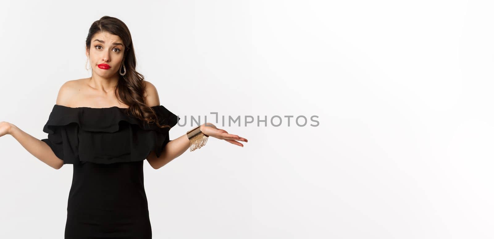 Fashion and beauty. Clueless attractive woman in black dress dont know, shrugging and smirking unaware, standing indecisive over white background.