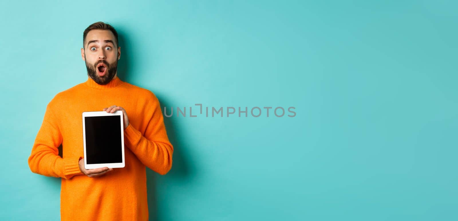 Technology. Surprised bearded man drop jaw, staring at camera and showing digital tablet screen, standing againt light blue background.