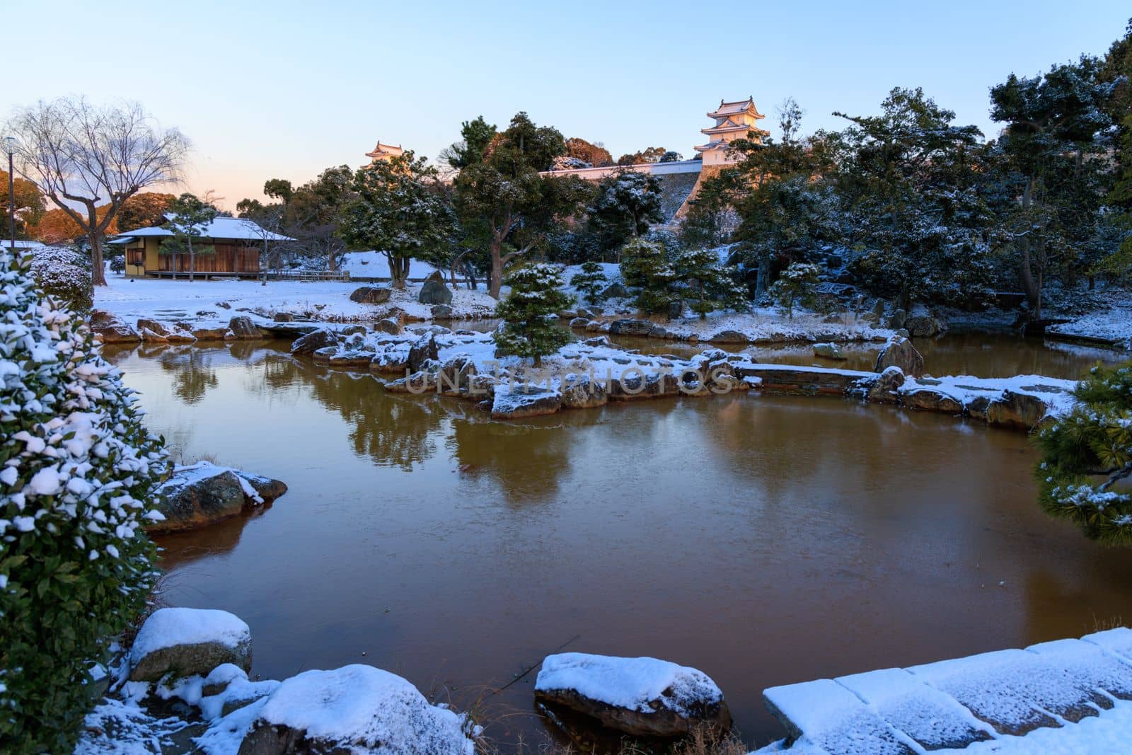Quiet pond in snow covered Japanese castle garden with golden sunrise light by Osaze