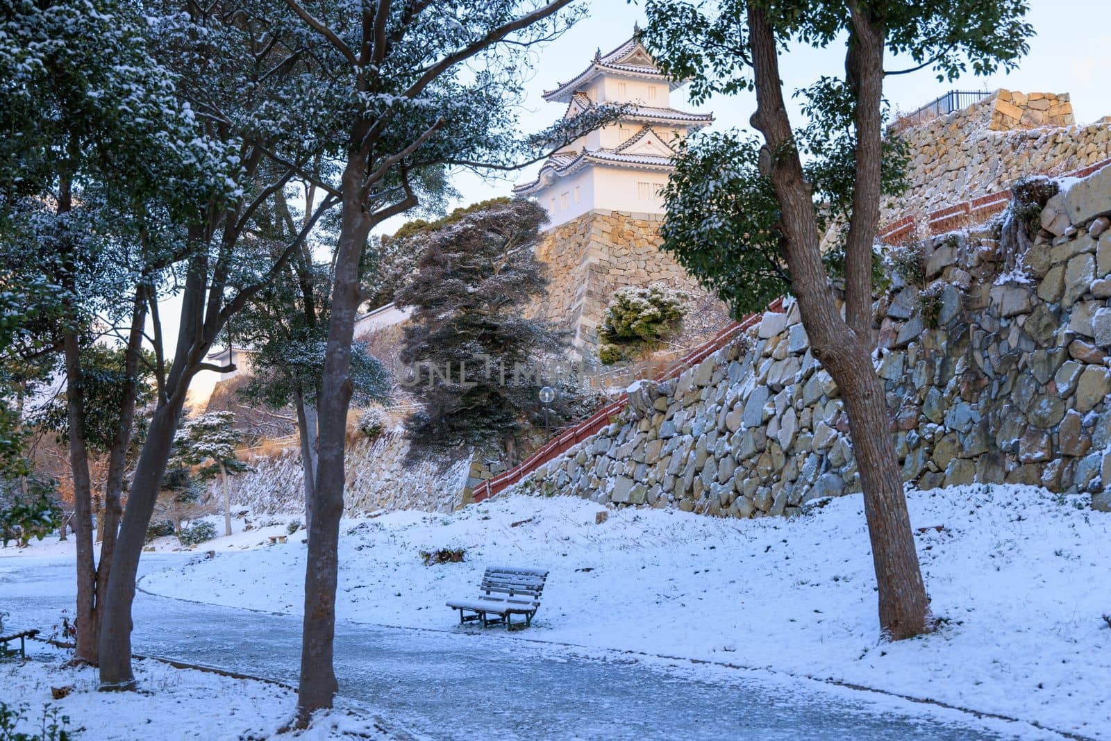 Snow covered bench at Japanese castle park on winter day by Osaze