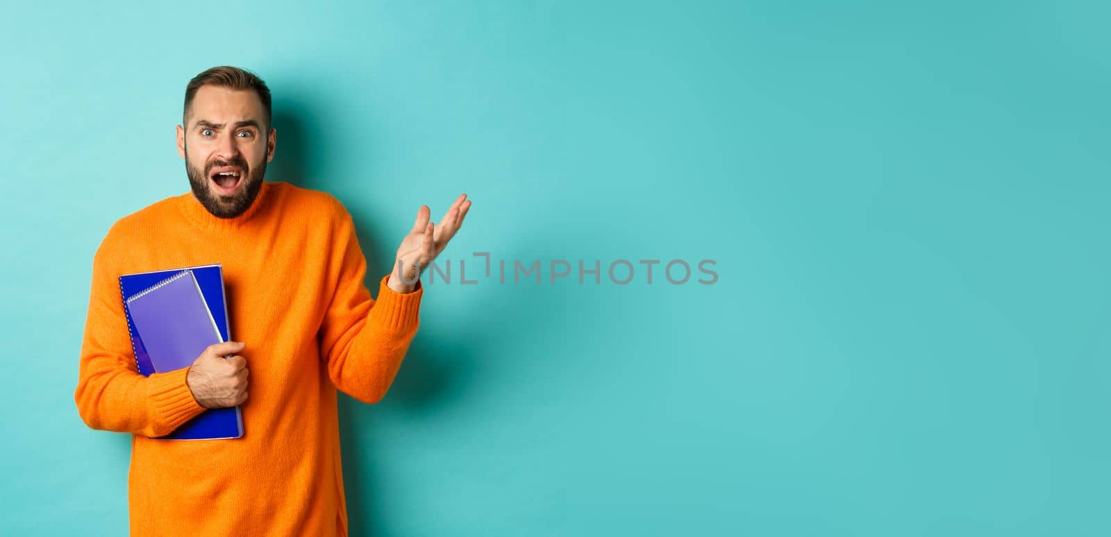 Education. Confused and disappointed man arguing, holding notebooks and complaining, standing over light blue background.