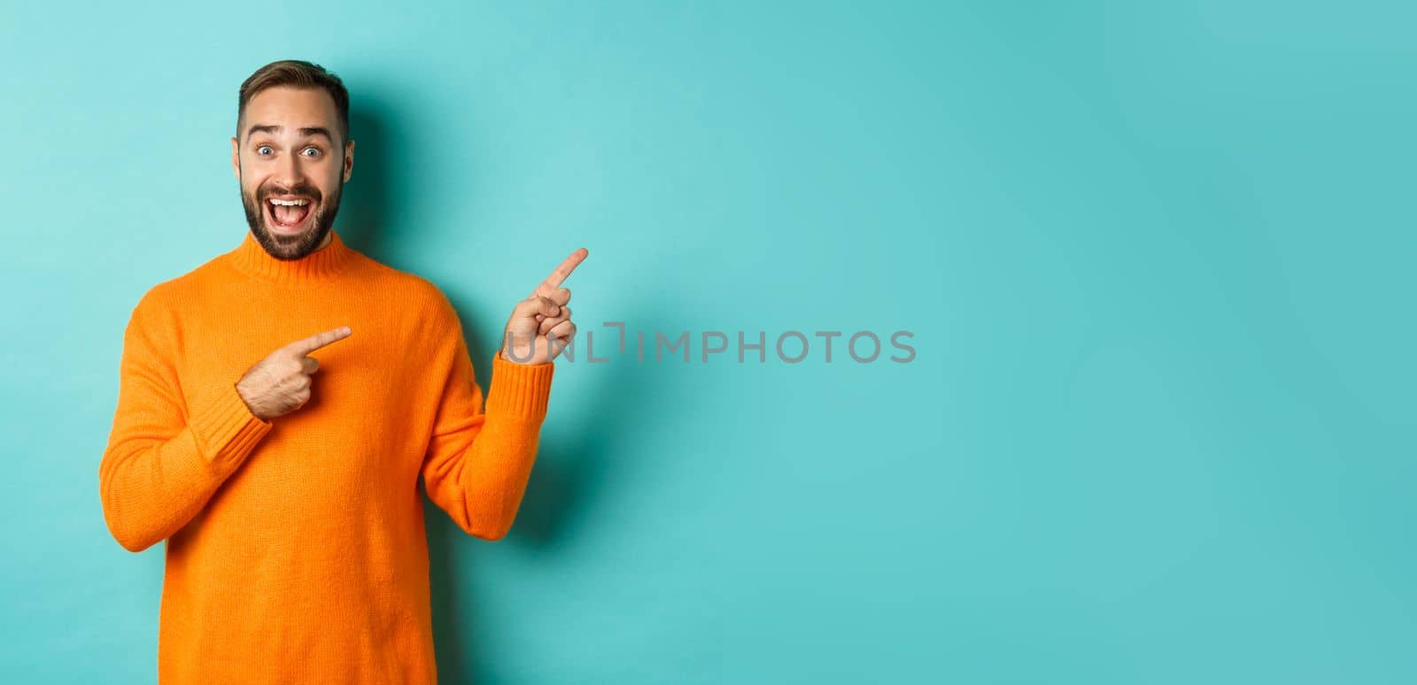 Excited man making an announcement, pointing fingers right your logo, standing over turquoise background.