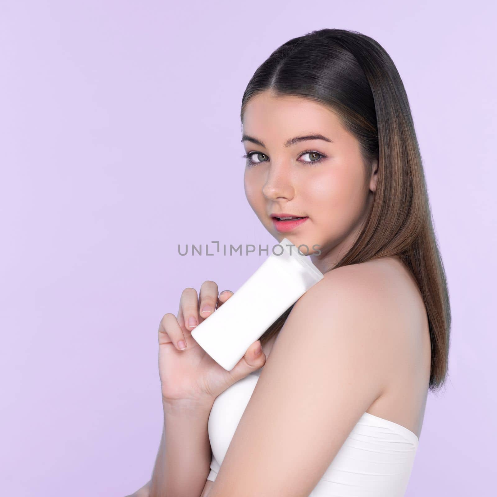 Young charming girl with natural beauty, perfect smooth skin hold lotion, cream, moisturizer tube. Beautiful girl show skincare product smiling on isolated background.
