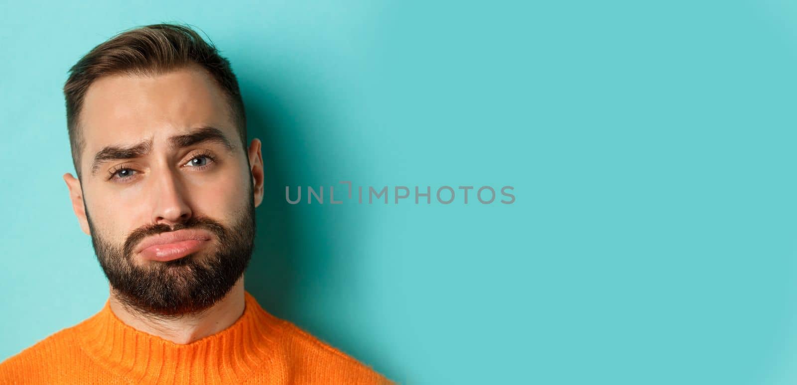 Headshot of sad and gloomy man complaining, pouting and frowning disappointed, standing against turquoise background by Benzoix