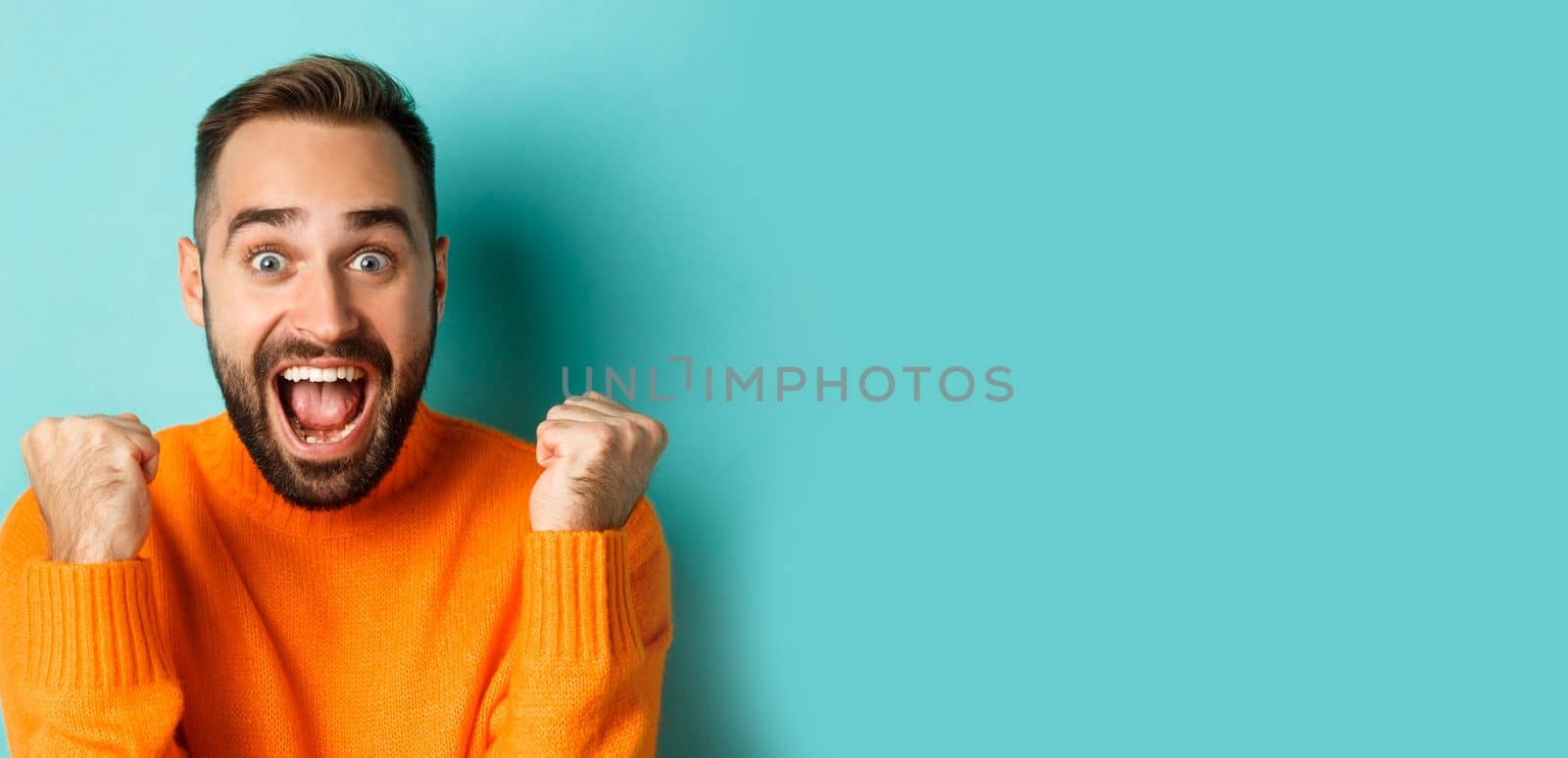 Image of handsome relieved man feeling satisfaction, rejoicing of winning or achievement, making fist pump and saying yes, standing over turquoise background by Benzoix