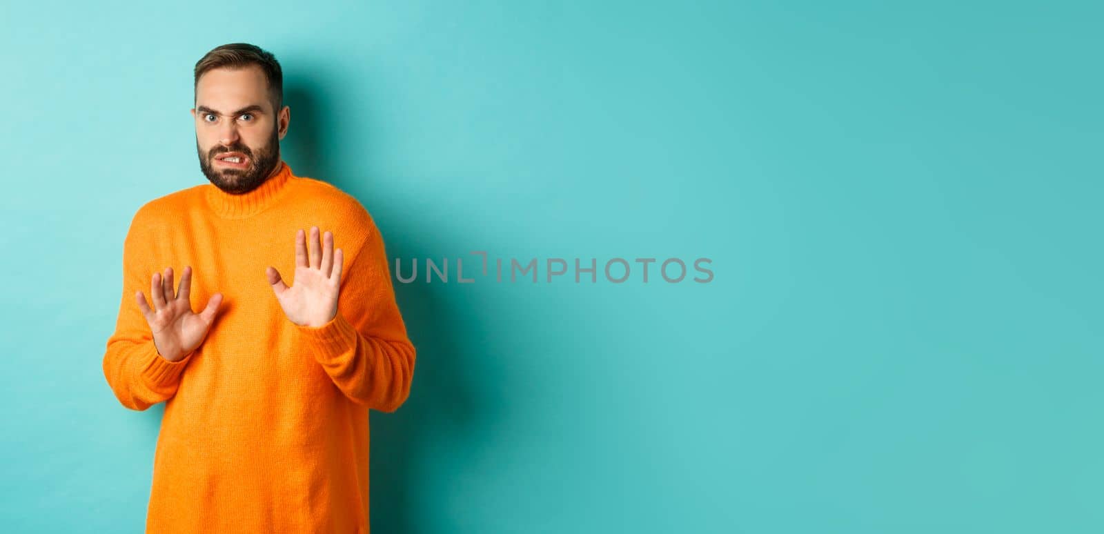 Alarmed guy shaking hands in rejection, declining and stepping away scared, standing over light blue background.