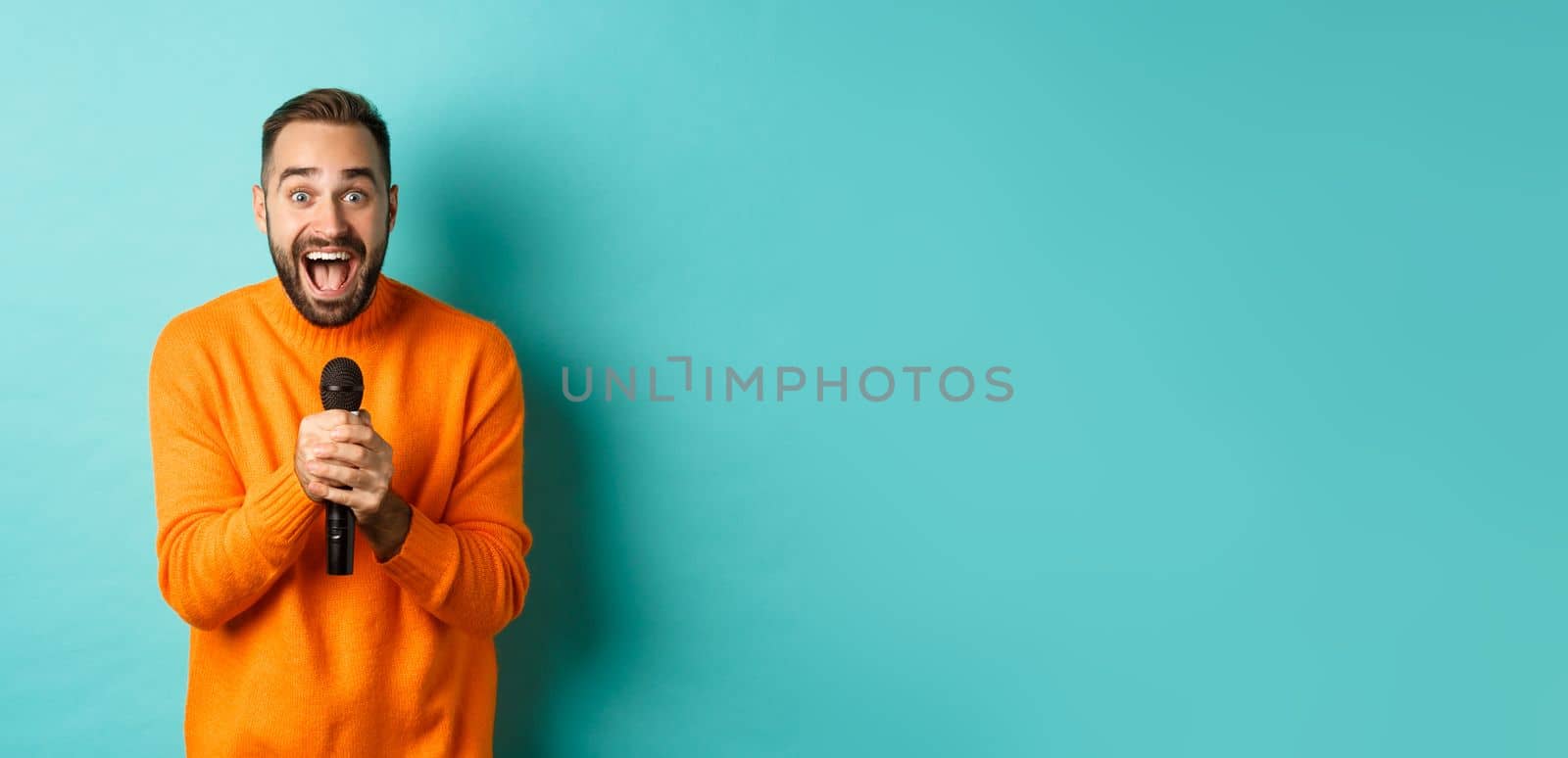 Handsome adult man perform song, singing into microphone, standing against turquoise background by Benzoix