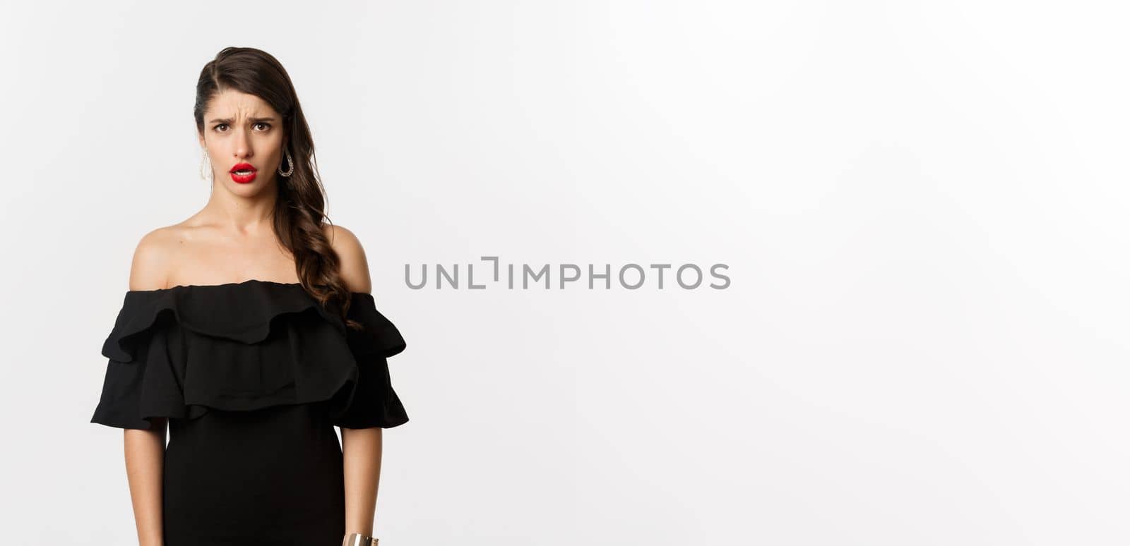 Fashion and beauty. Disappointed and upset woman in black dress staring at camera displeased, complaining with jealous look, standing over white background.