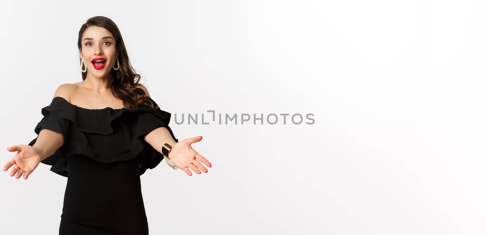 Fashion and beauty concept. Happy young woman in glamour black dress, reaching hands forward to take something, waiting for hug, white background.